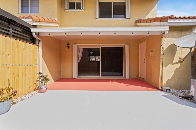 property entrance featuring a tiled roof, a patio area, fence, and stucco siding