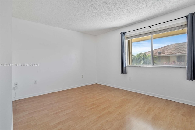 empty room featuring light wood-style floors, baseboards, and a textured ceiling