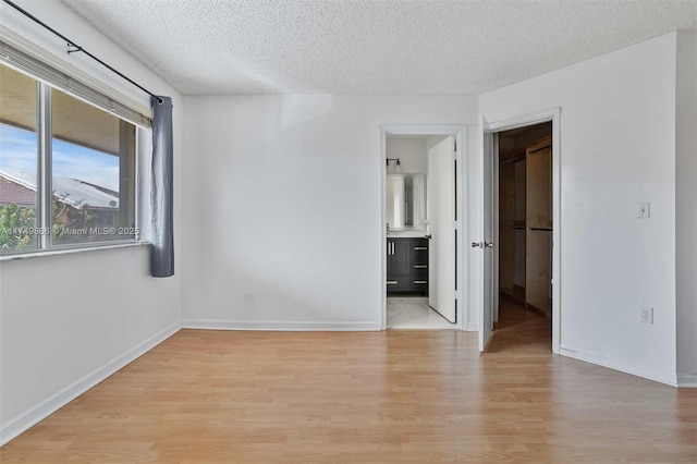 spare room featuring a textured ceiling, baseboards, and light wood-style floors