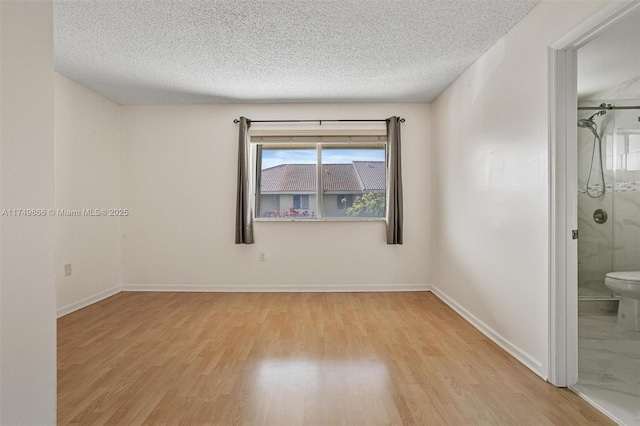 spare room with baseboards, a textured ceiling, and light wood finished floors