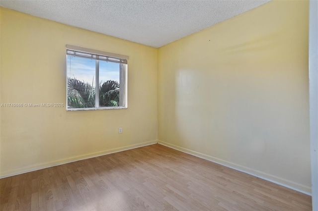 spare room with light wood-type flooring, a textured ceiling, and baseboards