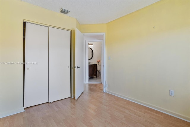 unfurnished bedroom with light wood-type flooring, a textured ceiling, visible vents, and a closet