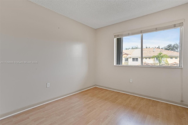 empty room with light wood-type flooring, a textured ceiling, and baseboards