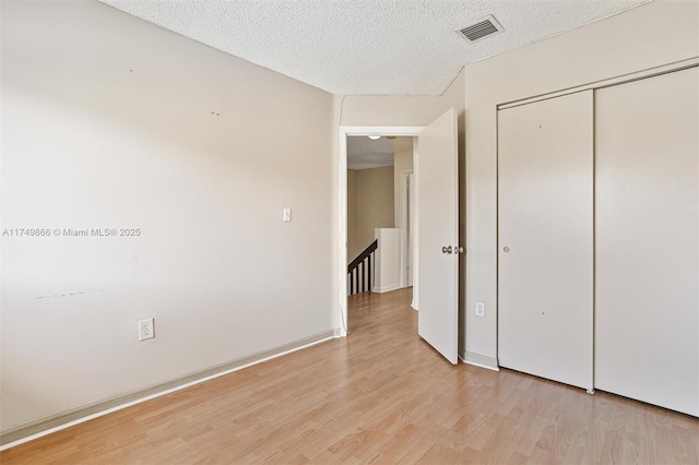 unfurnished bedroom featuring a closet, visible vents, a textured ceiling, and light wood finished floors