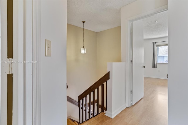 hall with light wood-style floors, baseboards, a textured ceiling, and an upstairs landing