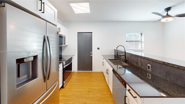 kitchen with stainless steel appliances, a sink, white cabinetry, and light wood-style floors