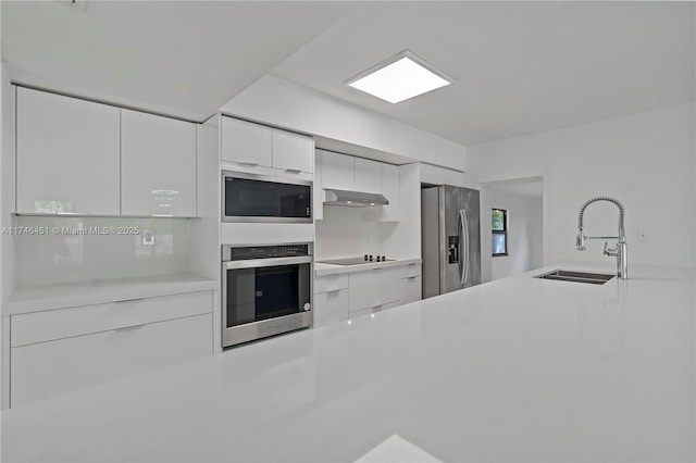 kitchen featuring under cabinet range hood, a sink, white cabinets, appliances with stainless steel finishes, and modern cabinets