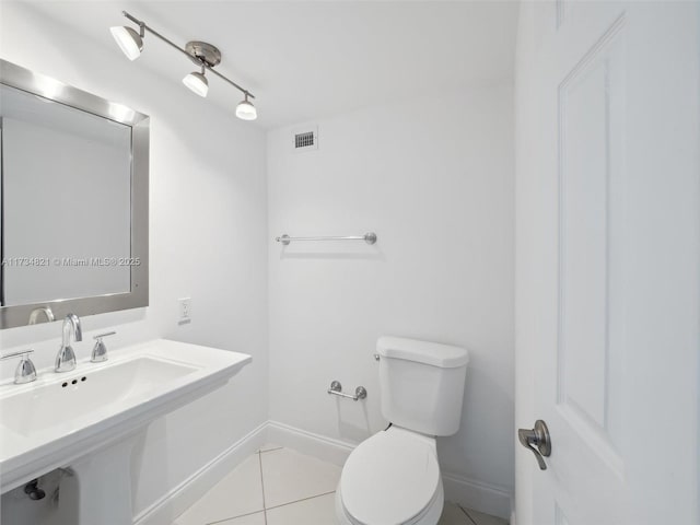 half bathroom featuring visible vents, baseboards, toilet, tile patterned floors, and a sink