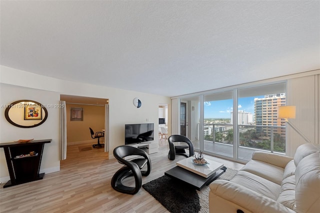 living area with a wall of windows, light wood-type flooring, a textured ceiling, and baseboards