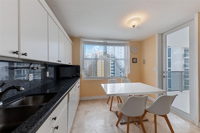 kitchen featuring a textured ceiling, a sink, baseboards, white cabinets, and backsplash