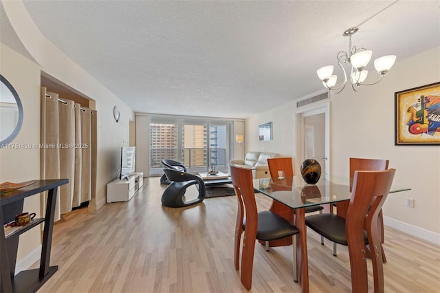 dining area featuring light wood-style floors, a notable chandelier, a textured ceiling, and baseboards