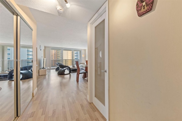 hallway with light wood-type flooring, floor to ceiling windows, a textured ceiling, and french doors