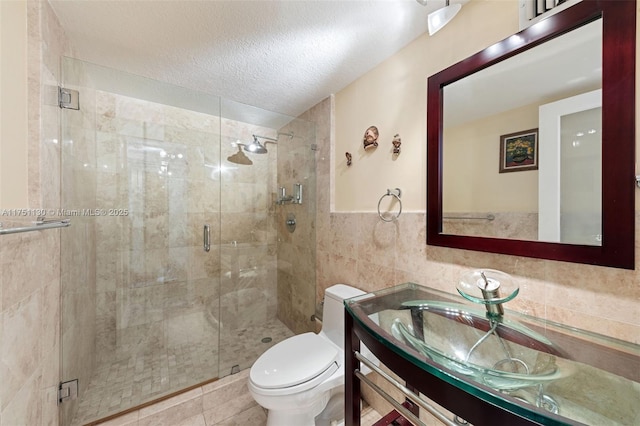 full bath featuring tile walls, toilet, a stall shower, a textured ceiling, and vanity