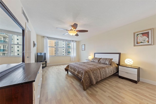 bedroom with visible vents, light wood-style floors, a ceiling fan, a textured ceiling, and baseboards