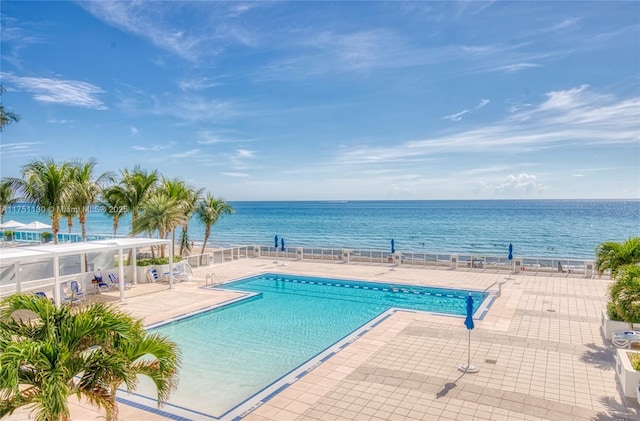 community pool with a water view, a patio area, and fence