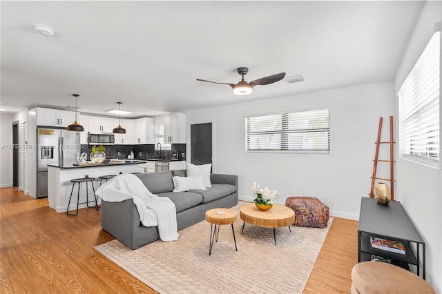 living room with baseboards, light wood finished floors, visible vents, and a ceiling fan