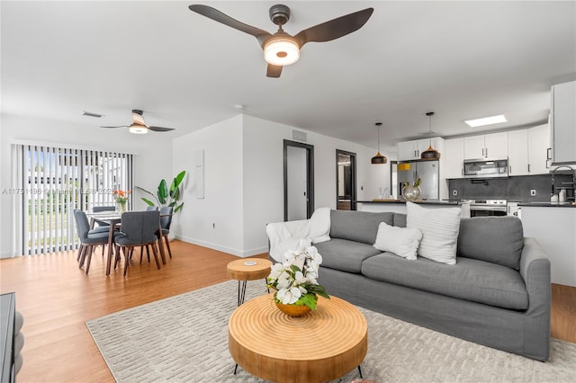 living area with a ceiling fan, baseboards, visible vents, and light wood finished floors