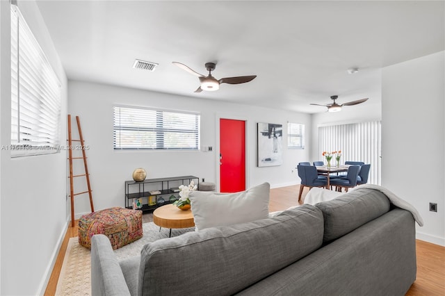 living area featuring light wood-style flooring, visible vents, ceiling fan, and baseboards