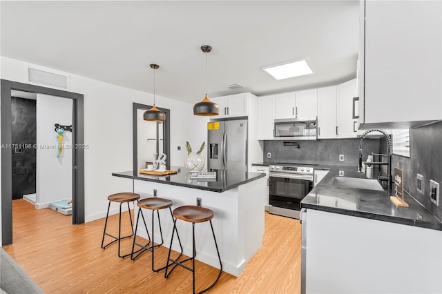 kitchen with pendant lighting, dark countertops, appliances with stainless steel finishes, white cabinetry, and a sink