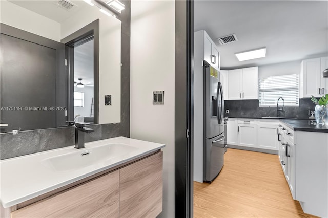 kitchen with stainless steel fridge, visible vents, dark countertops, white cabinetry, and a sink