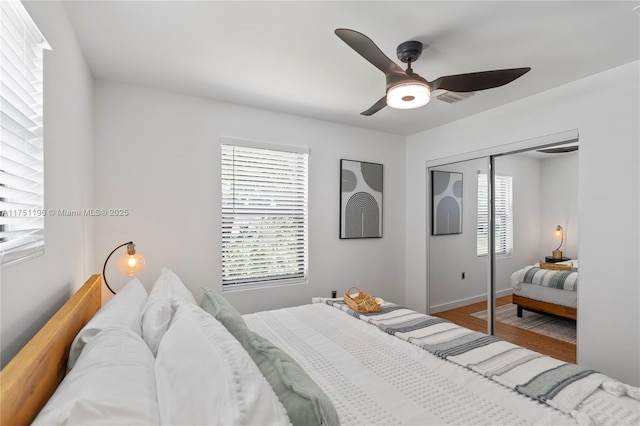 bedroom featuring ceiling fan, a closet, multiple windows, and wood finished floors