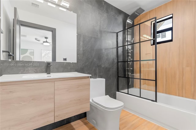 full bathroom featuring visible vents, toilet, enclosed tub / shower combo, vanity, and tile walls