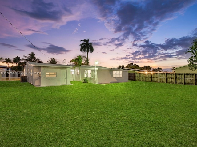 back of house at dusk with a yard, an outdoor structure, a fenced backyard, and stucco siding