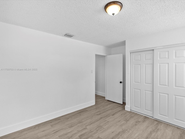 unfurnished bedroom featuring baseboards, visible vents, light wood-style flooring, a textured ceiling, and a closet