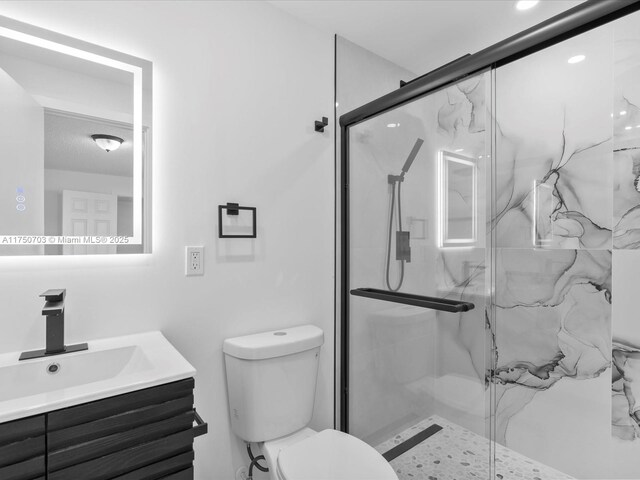 bathroom featuring toilet, a marble finish shower, and vanity