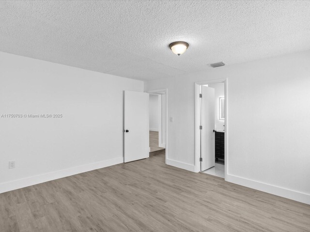 unfurnished bedroom featuring visible vents, ensuite bathroom, a textured ceiling, wood finished floors, and baseboards