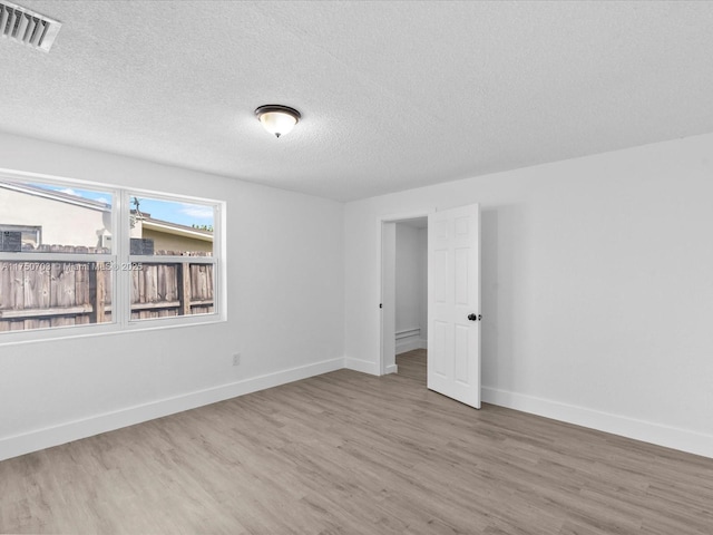 spare room with a textured ceiling, wood finished floors, visible vents, and baseboards