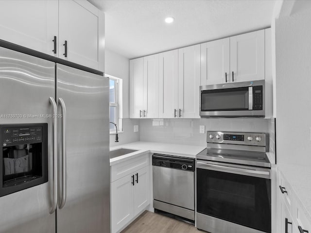 kitchen with stainless steel appliances, tasteful backsplash, a sink, and white cabinets