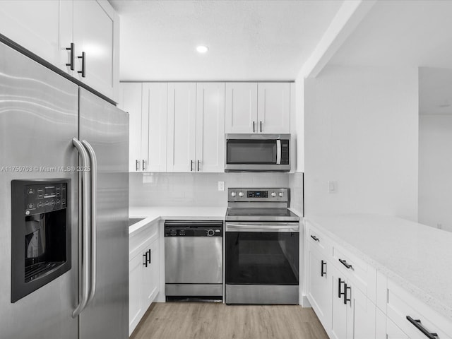 kitchen with stainless steel appliances, white cabinets, light wood-style floors, light countertops, and decorative backsplash