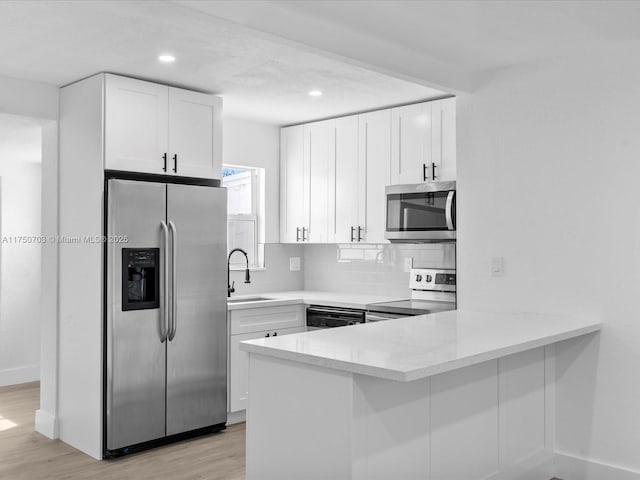 kitchen featuring stainless steel appliances, white cabinetry, a sink, and a peninsula