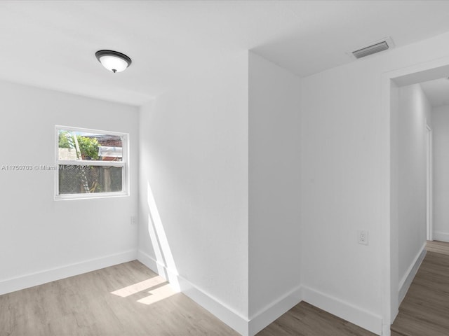 spare room with wood finished floors, visible vents, and baseboards