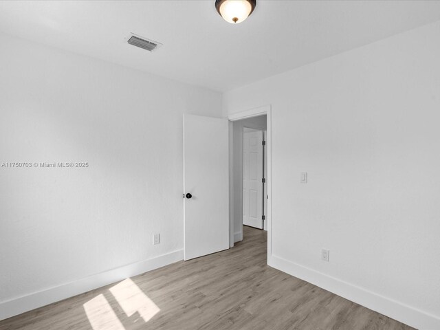 spare room featuring light wood-type flooring, visible vents, and baseboards