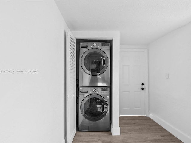 laundry room with laundry area, wood finished floors, stacked washer and clothes dryer, and baseboards