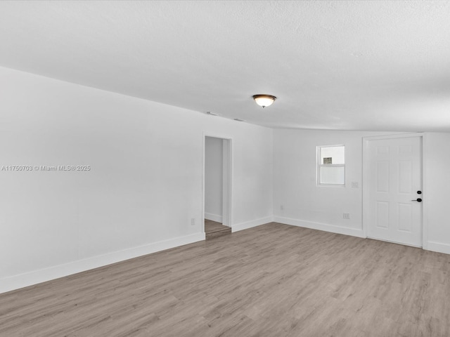 empty room with a textured ceiling, light wood finished floors, and baseboards