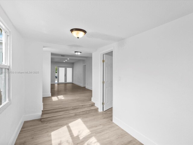 hall with light wood-type flooring, baseboards, and french doors