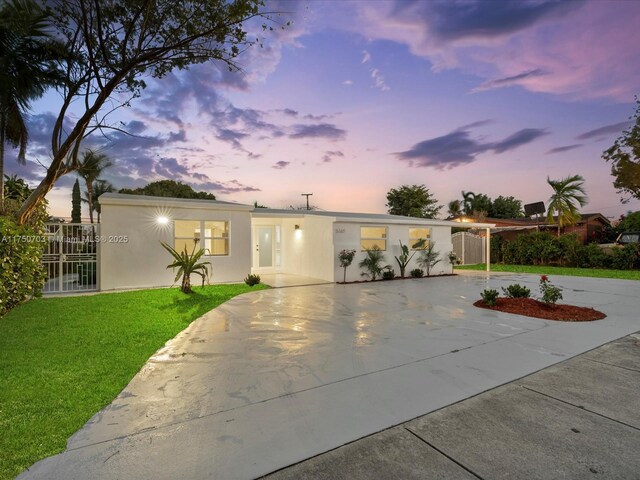 view of front of house featuring concrete driveway, a lawn, fence, and stucco siding