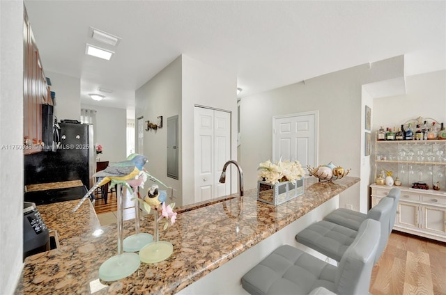 kitchen with electric panel, light stone countertops, a kitchen bar, and light wood finished floors