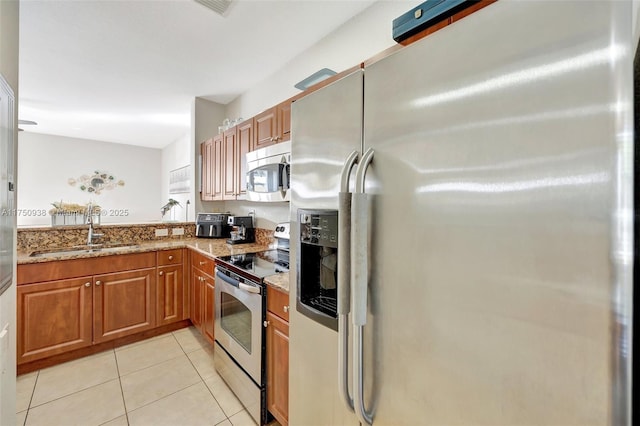 kitchen with light tile patterned flooring, light stone countertops, stainless steel appliances, a sink, and brown cabinets