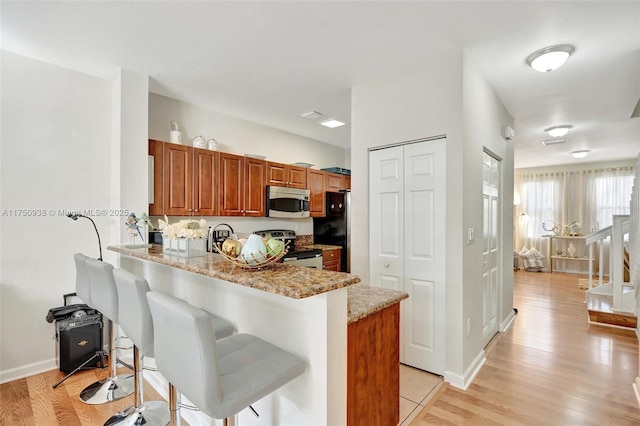 kitchen with brown cabinetry, a kitchen breakfast bar, a peninsula, light stone countertops, and stainless steel appliances