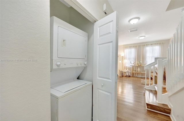 laundry area featuring laundry area, a textured wall, stacked washing maching and dryer, and wood finished floors