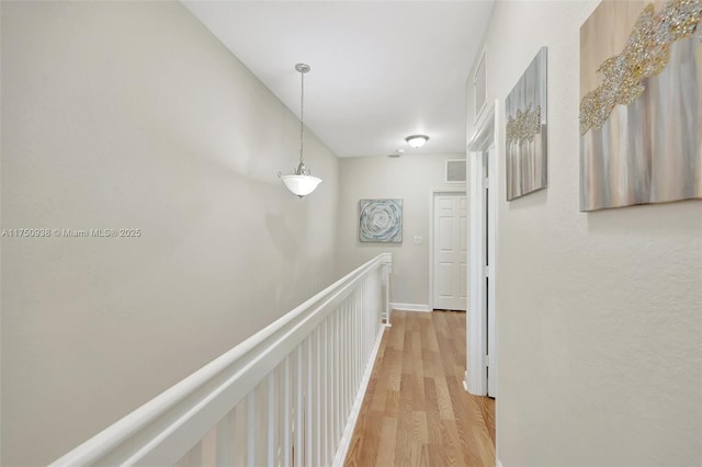 hallway featuring light wood-type flooring, wainscoting, a decorative wall, and visible vents