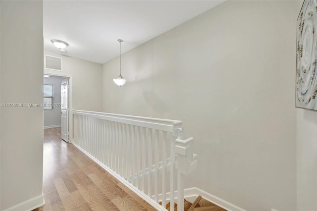 hall featuring light wood finished floors, baseboards, visible vents, and an upstairs landing