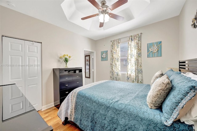 bedroom with baseboards, a raised ceiling, a ceiling fan, wood finished floors, and a closet