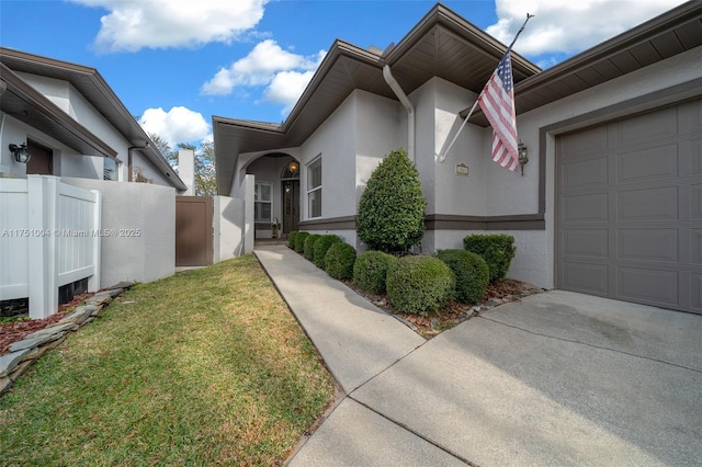 exterior space with a lawn, an attached garage, fence, and stucco siding