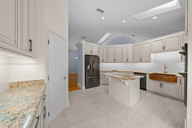 kitchen featuring a breakfast bar, a center island, light stone countertops, black appliances, and a sink