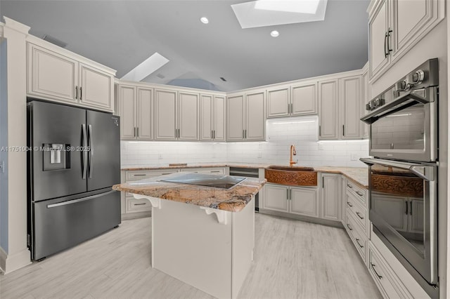 kitchen featuring a kitchen island, a breakfast bar area, light stone countertops, stainless steel appliances, and a sink